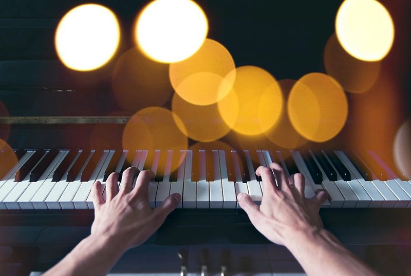 Manos interpretando el piano con luces cálidas de fondo